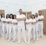 Zespół stomatologów w białych uniformach stoi w rzędzie, z rękami skrzyżowanymi na piersi.