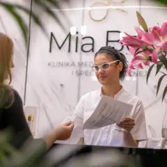 Recepcjonistka w klinice dermatologicznej podaje dokumenty klientce.
